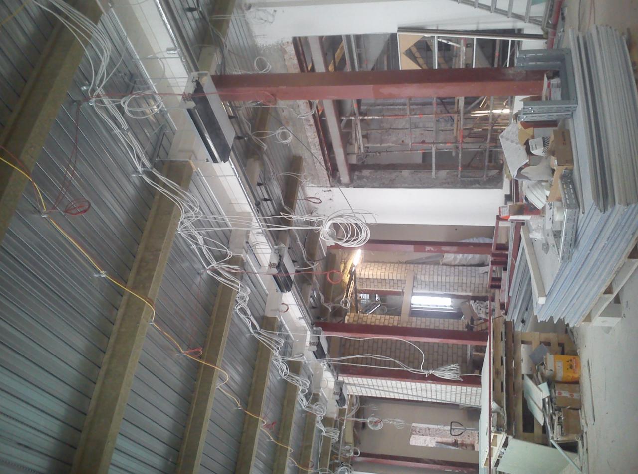 Montaż instalacji elektrycznej w budynku w trakcie prac wykończeniowych, widoczne kable, profile metalowe i materiały izolacyjne.