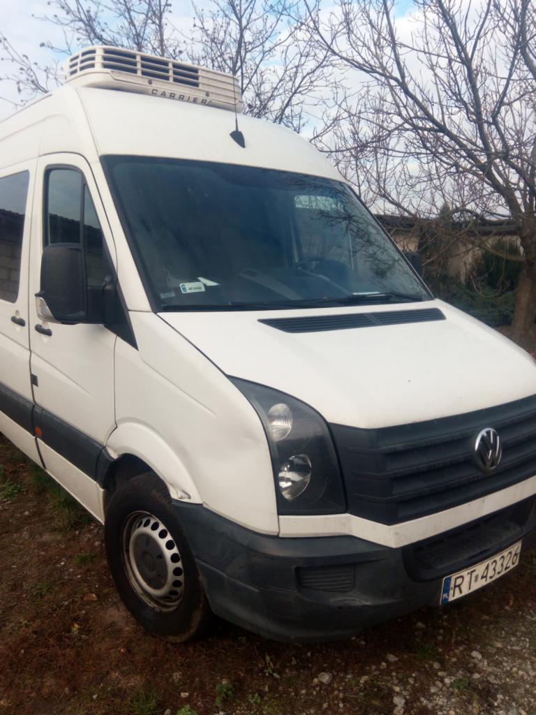 Biały samochód dostawczy Volkswagen Crafter z agregatem chłodniczym na dachu, zaparkowany na ziemi z widocznymi drzewami w tle.