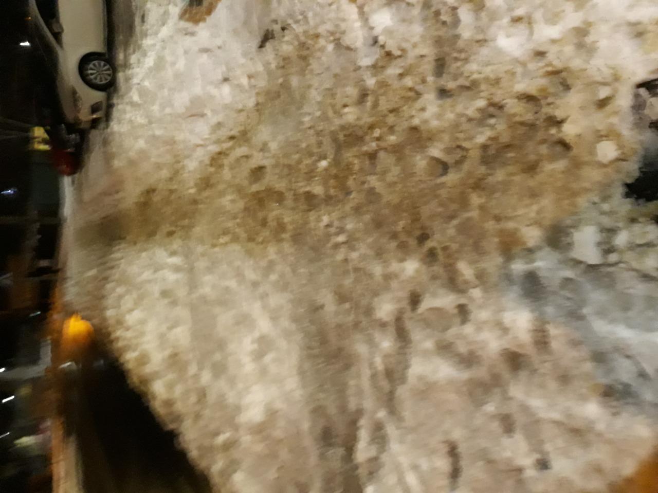 Śnieg z lodem zalegający na brukowanej powierzchni, widoczny fragment samochodu w tle.