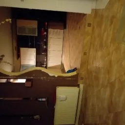 Kuchnia w trakcie remontu: widoczne przygotowane ściany do dalszych prac, zamontowane meble kuchenne i grzejnik, brązowe płytki na podłodze i ścianie.