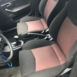 pranietapicerki-bydgoszcz - Wnętrze samochodu z czarno-różową tapicerką foteli. Widoczne fotele przednie, kierownica i dźwignia zmiany biegów. Ciemne wnętrze pojazdu.