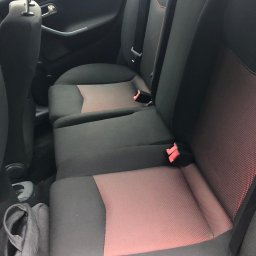 pranietapicerki-bydgoszcz - Czarne fotele samochodowe z czerwonymi wstawkami, widok z tyłu, pasy bezpieczeństwa, torba leżąca na podłodze. Wnętrze pojazdu.