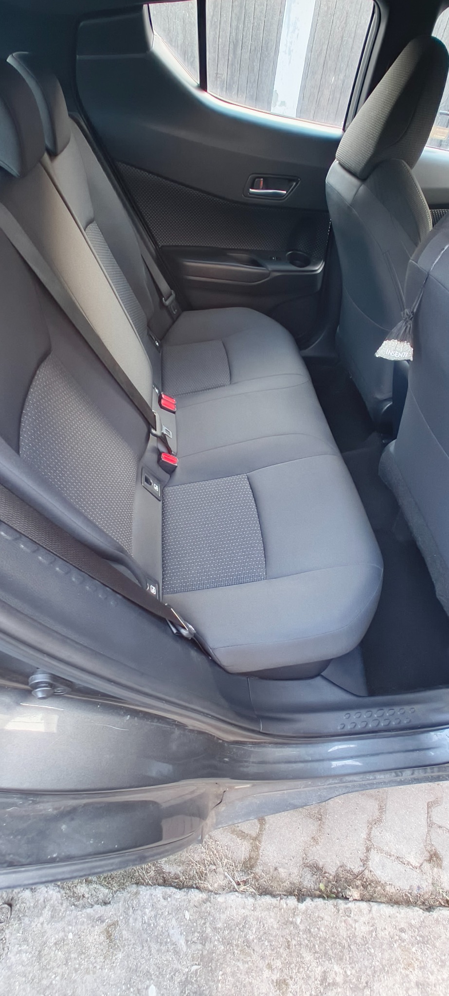 Wnętrze samochodu z otwartymi drzwiami ukazuje tylną kanapę z szarej tapicerki. Widoczne pasy bezpieczeństwa i zagłówki. Czyste, zadbane wnętrze pojazdu.