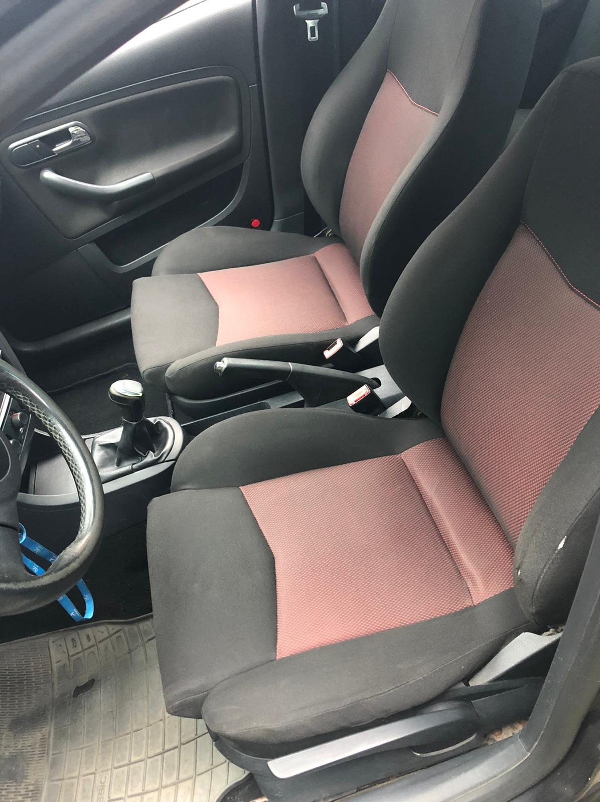 Wnętrze samochodu z czarno-różową tapicerką foteli. Widoczne fotele przednie, kierownica i dźwignia zmiany biegów. Ciemne wnętrze pojazdu.