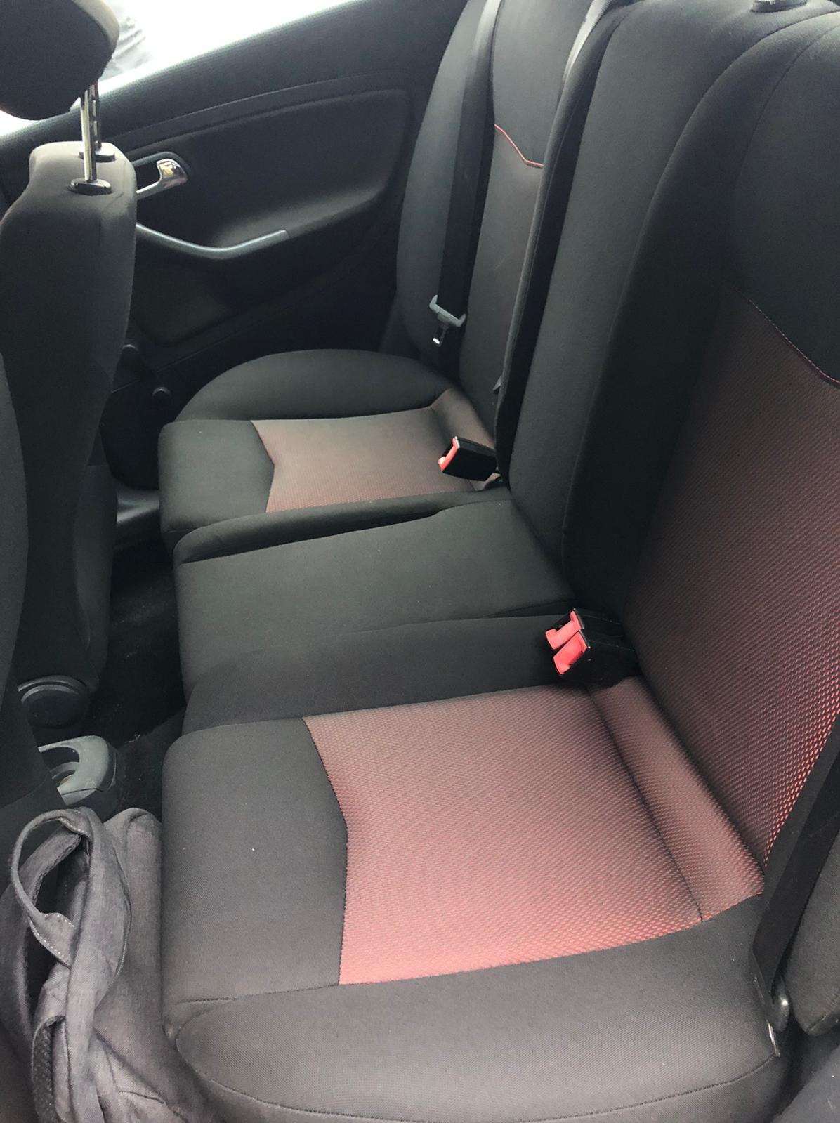 Czarne fotele samochodowe z czerwonymi wstawkami, widok z tyłu, pasy bezpieczeństwa, torba leżąca na podłodze. Wnętrze pojazdu.