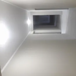 Pomalowane na jasny kolor ściany klatki schodowej widziane z dołu, z widocznymi poziomami wyżej i wpadającym światłem.