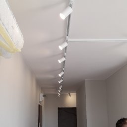 ELEKTROMIX Łukasz Rudziński - Zamontowane białe reflektory szynowe na suficie w korytarzu, widoczne ślady prac wykończeniowych.