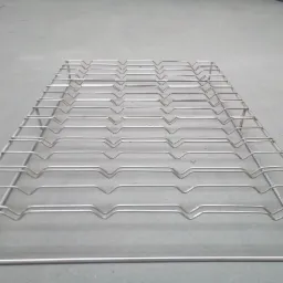 Metalowa krata z drutu, spawana w regularne prostokąty z półokrągłymi wgłębieniami, leżąca na szarej powierzchni.