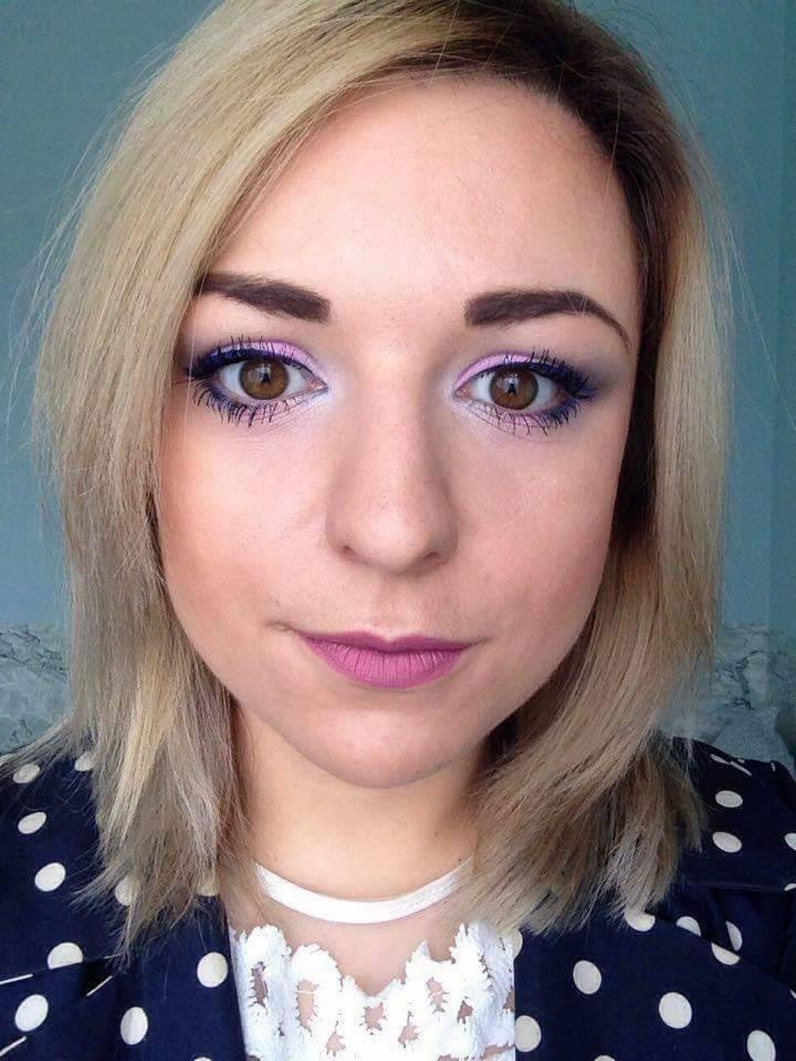 Portret kobiety z fioletowym makijażem oczu i ust, w bluzce w grochy i białym chokerze.