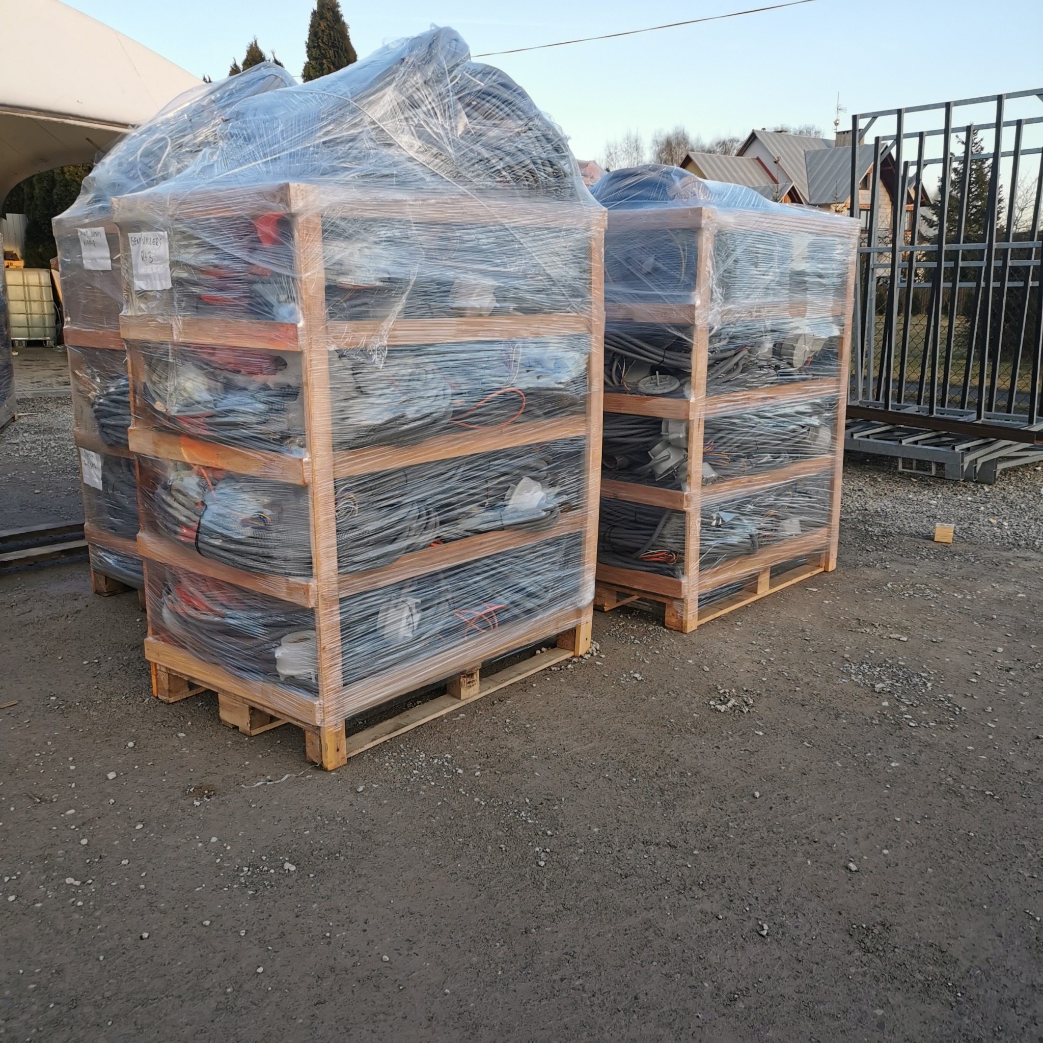 Palety z zapakowanymi w folie elementami oświetlenia, prawdopodobnie lampami, przygotowane do transportu na zewnątrz.