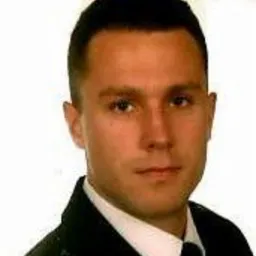 Portret mężczyzny w koszuli, z krótkimi włosami, na jasnym tle. Zdjęcie o obniżonej jakości.