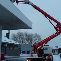 Firma Usługowa WIKTER Łukasz Czopek - Czerwony podnośnik koszowy przy białym zadaszeniu stacji benzynowej, widoczne pomarańczowe pachołki drogowe i numer telefonu kontaktowego.