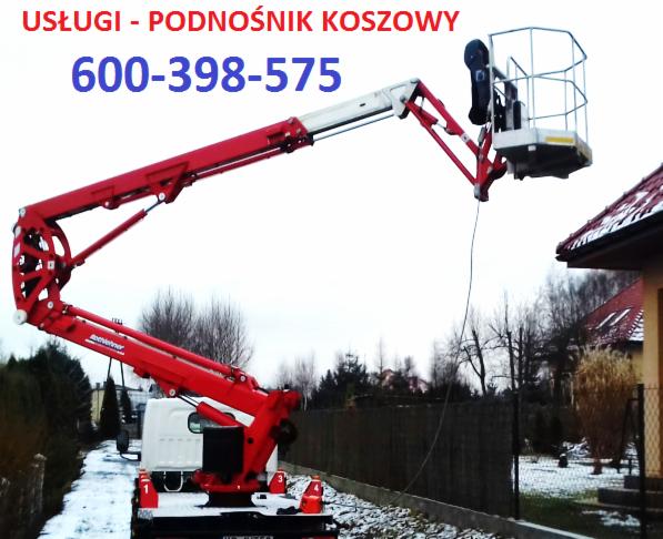 Czerwony podnośnik na białym samochodzie dostawczym, wysięgnik uniesiony w kierunku dachu domu, widoczne drzewa w tle.