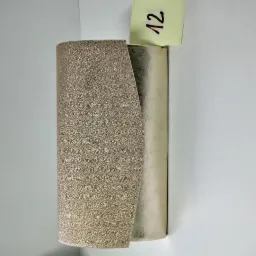 Złoty, teksturowany skórzany element dekoracyjny, częściowo zakrywający srebrny cylinder, z żółtą karteczką z numerem '12' na górze, na białym tle.