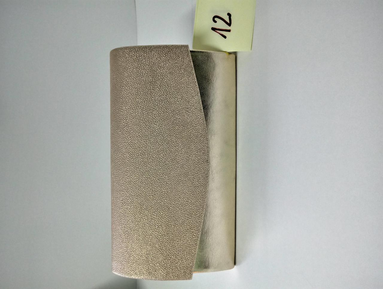 Złoty, teksturowany skórzany element dekoracyjny, częściowo zakrywający srebrny cylinder, z żółtą karteczką z numerem '12' na górze, na białym tle.