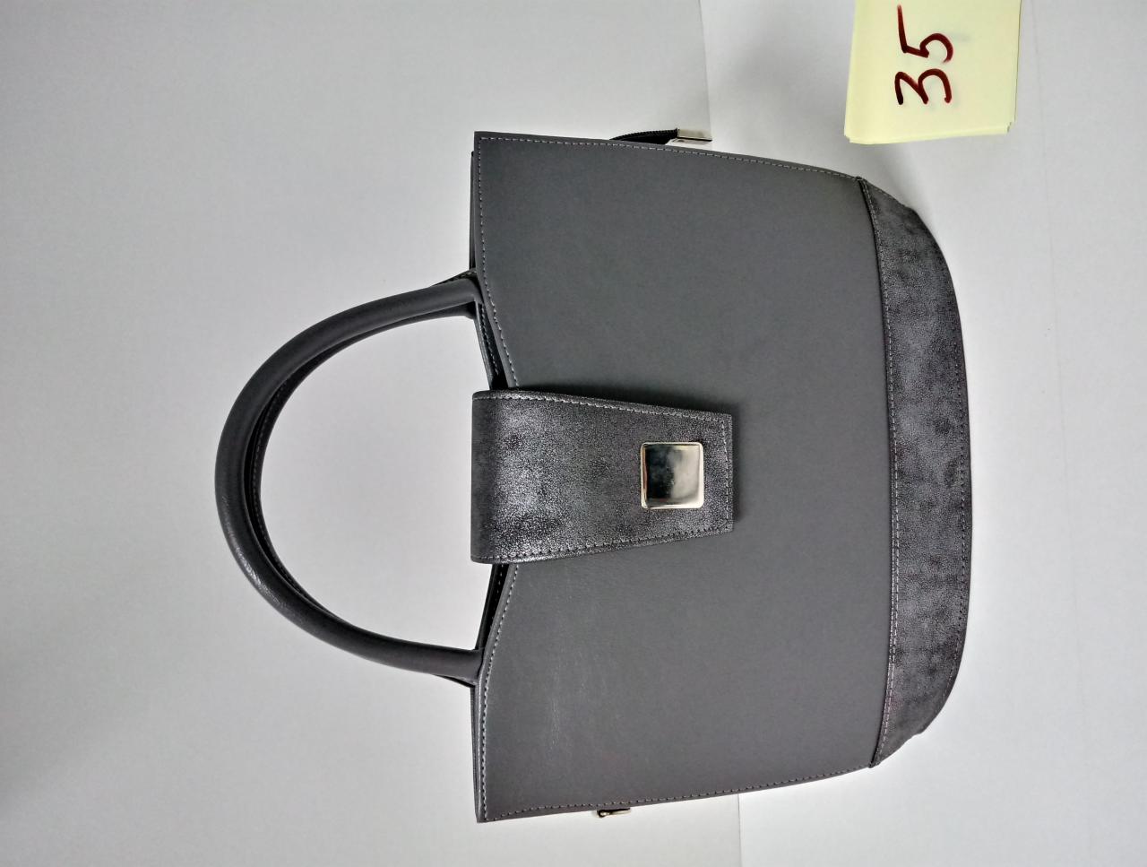 Szara torebka damska z czarnymi uchwytami i zapięciem, widoczna kartka z numerem 35 w tle.