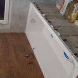 Remonty - Biały brodzik w trakcie montażu w łazience, widoczne worki z klejem do płytek, drewnopodobne panele podłogowe i fragment okna.