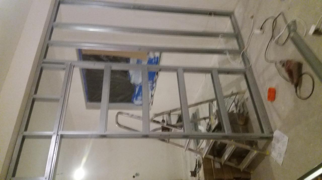 Metalowa konstrukcja ścianki działowej w trakcie montażu, widoczna drabina i narzędzia, pomieszczenie w stanie surowym.