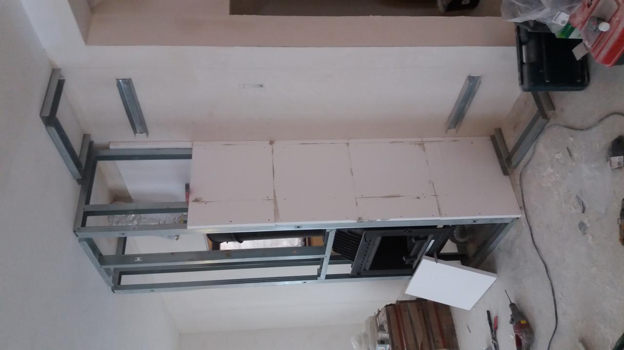 Sufit podwieszany w trakcie montażu: metalowa konstrukcja szkieletowa, częściowo obłożona płytami gipsowo-kartonowymi, widoczny otwór na oświetlenie lub wentylację.