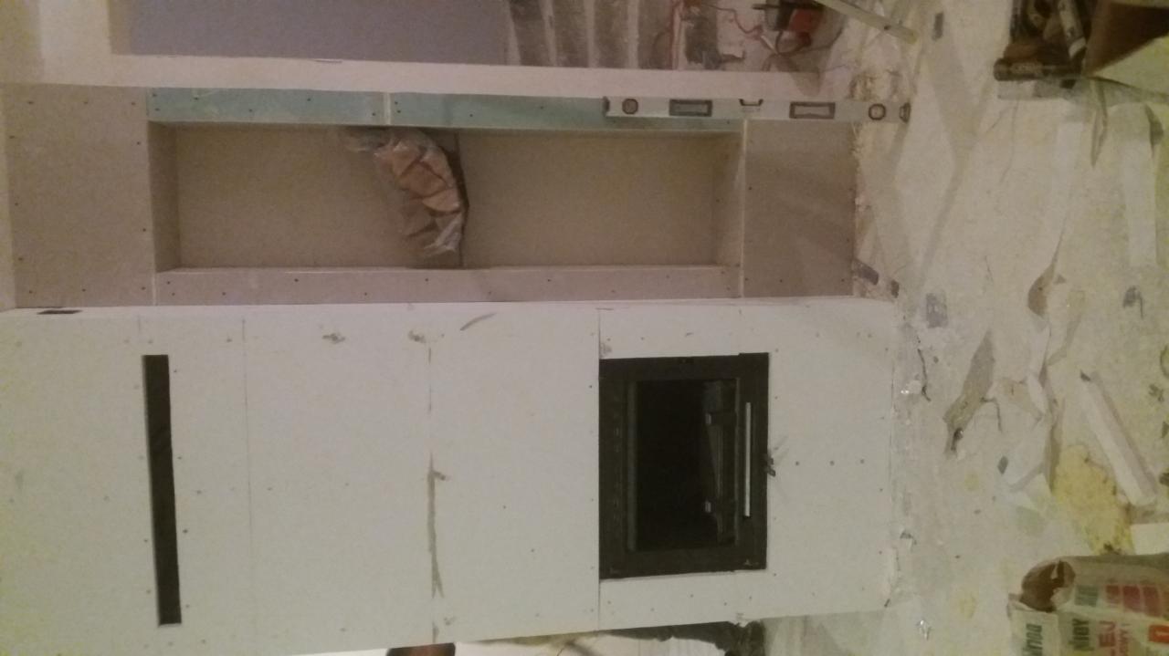 Wnęka w ścianie z zamontowanym wkładem kominkowym, w trakcie obudowy płytami gipsowo-kartonowymi, widoczne ślady po starym tapetowaniu na ścianie.