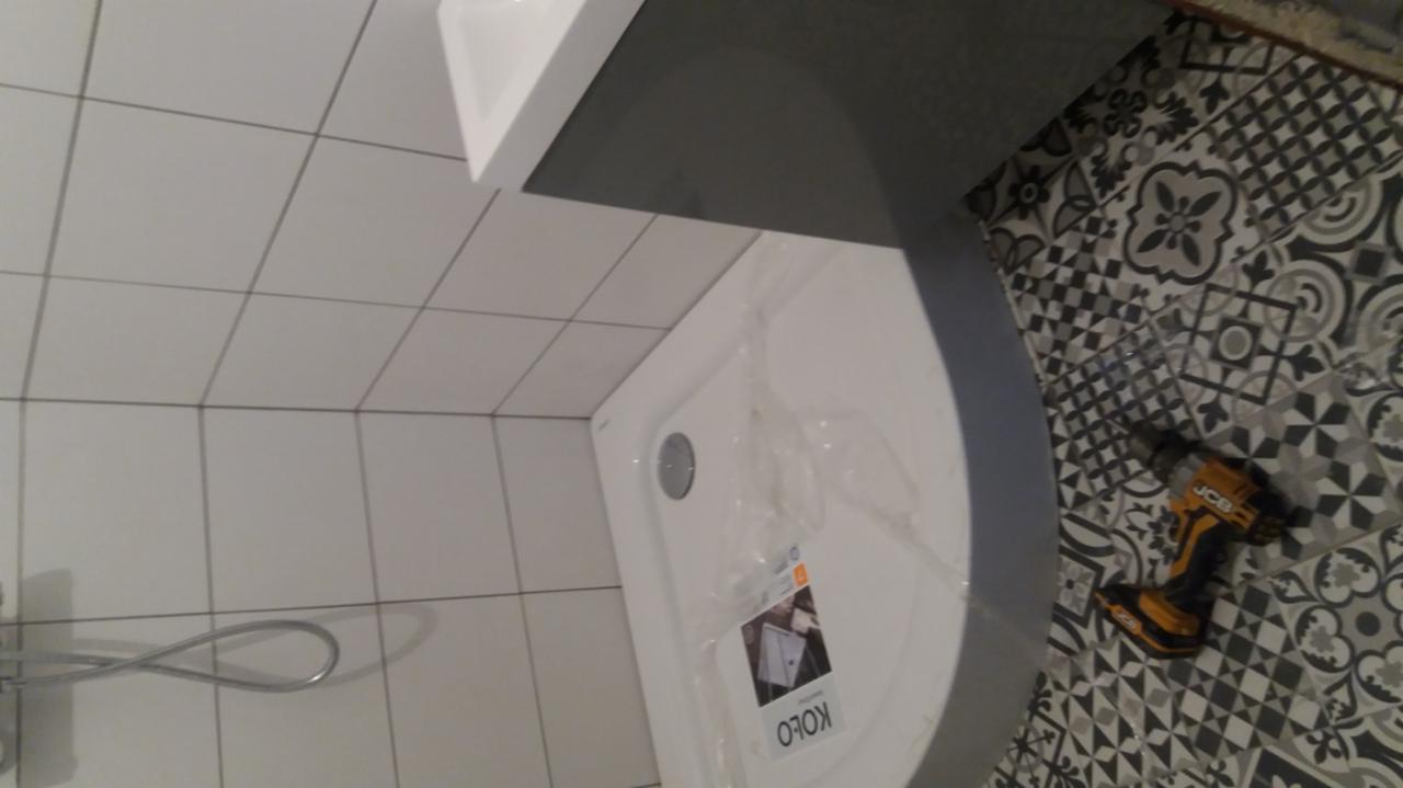 Montaż kabiny prysznicowej KOLO w łazience w Tokarni, widoczna wiertarka JCB na wzorzystych płytkach podłogowych, białe płytki ścienne i chromowana słuchawka prysznicowa.