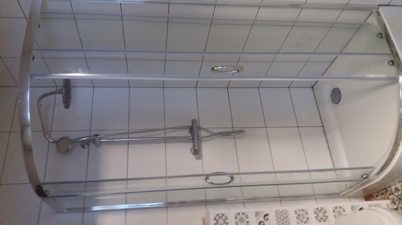 Kabina prysznicowa z przesuwnymi drzwiami, widoczne białe płytki na ścianach i chromowana bateria z deszczownicą, ujęcie z dołu.