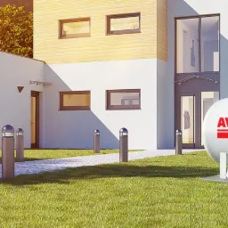 Biały zbiornik LPG marki Avia umieszczony na betonowej podstawie przed nowoczesnym domem z jasną elewacją i szarym dachem, oświetlony popołudniowym słońcem.