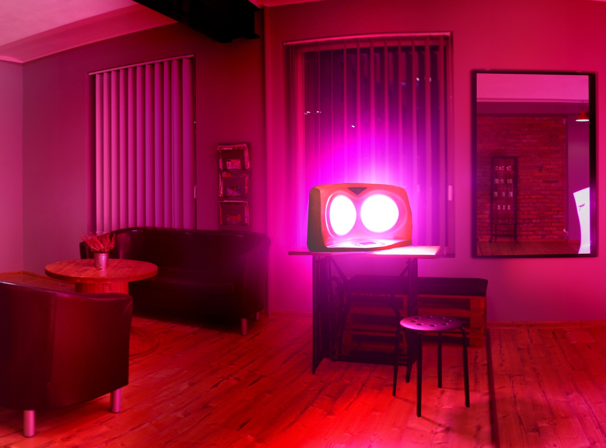 Pokój z lampą kolagenową emitującą intensywne różowe światło, widoczne meble w tle, w tym sofa i stolik kawowy, oraz okno z pionowymi żaluzjami.