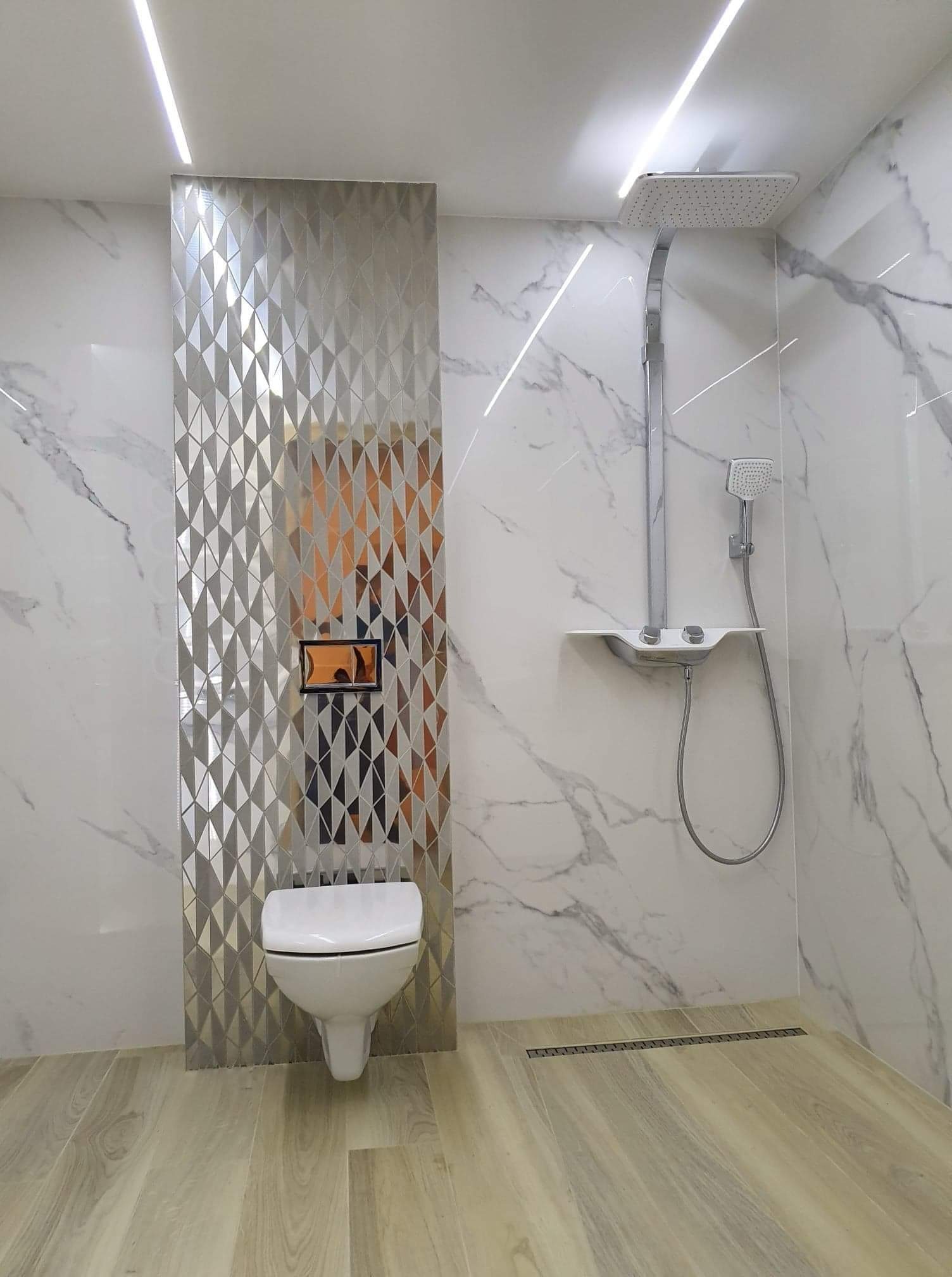 Nowoczesna łazienka z marmurowymi płytkami, geometryczną mozaiką za toaletą, deszczownicą i drewnopodobną podłogą z odpływem liniowym.