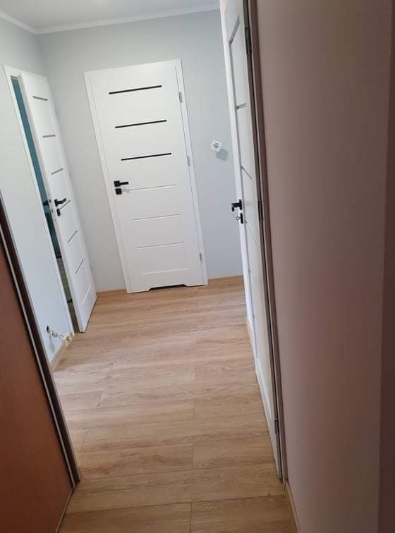 Korytarz po remoncie z trzema białymi drzwiami z czarnymi klamkami i panelami podłogowymi imitującymi drewno.