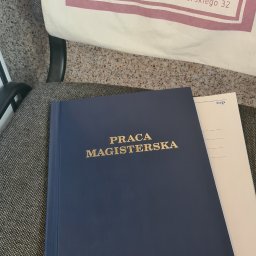 LUMEN - Oprawiona praca magisterska z napisem w kolorze złotym leży na krześle obok torby z logo biura tłumaczeń Lumen, oferującego tłumaczenia zwykłe i przysięgłe.
