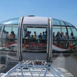 Kapsuła diabelskiego młyna z pasażerami w trakcie przejażdżki, widok na panoramę miasta i rzekę z góry.