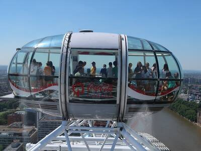 Kapsuła diabelskiego młyna z pasażerami w trakcie przejażdżki, widok na panoramę miasta i rzekę z góry.