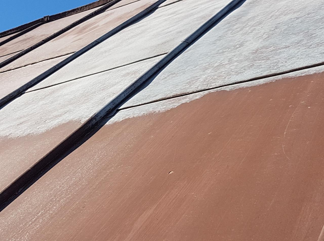 Częściowo oczyszczony, brązowy dach z blachy trapezowej, z widoczną warstwą białego nalotu i pozostałości zabrudzeń na górnej części.