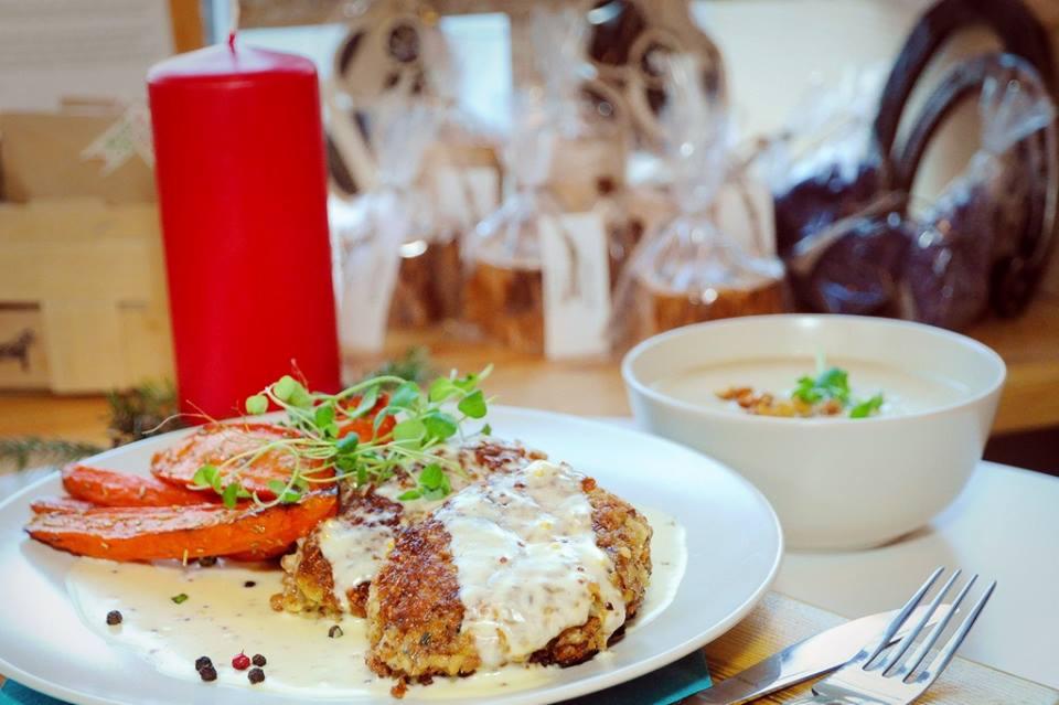 Uroczysta kolacja: kotlety w sosie śmietanowym, pieczona marchewka, zupa krem w białej miseczce, czerwona świeca i zapakowane prezenty w tle.