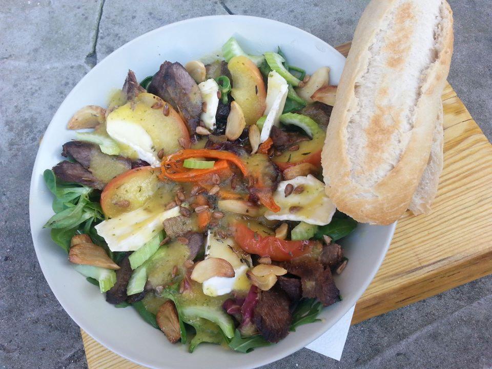 Sałatka z grillowaną wołowiną, jabłkami, serem camembert, selerem naciowym i sosem na bazie ziaren słonecznika, podana z bagietką na drewnianej desce.