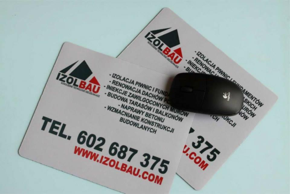 Dwie wizytówki firmy izolacyjnej IZOLBAU z myszką komputerową Logitech na wierzchu, prezentujące zakres usług i dane kontaktowe.