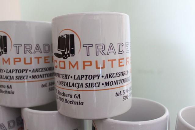 Białe kubki z nadrukowanym logo firmy komputerowej, prezentujące usługi: komputery, laptopy, akcesoria, instalacja sieci, monitoring oraz dane kontaktowe.