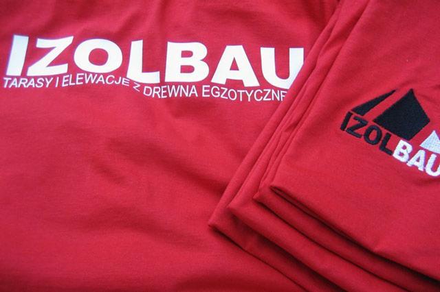 Czerwona koszulka z nadrukowanym białym logo firmy IZOLBAU, specjalizującej się w tarasach i elewacjach z drewna egzotycznego, oraz wyhaftowanym logo na rękawie.