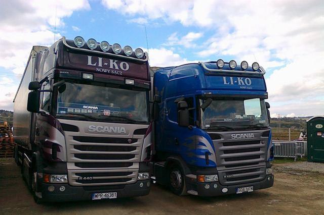 Dwa samochody ciężarowe Scania w kolorach bordowym i niebieskim z logo firmy LI-KO i nazwą miejscowości Nowy Sącz na kabinach, stojące obok siebie na placu.
