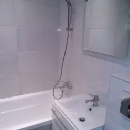 Nowoczesna łazienka z białą wanną, umywalką z szafką i lustrem z podświetleniem LED, wykończona jasnymi, prostokątnymi płytkami.