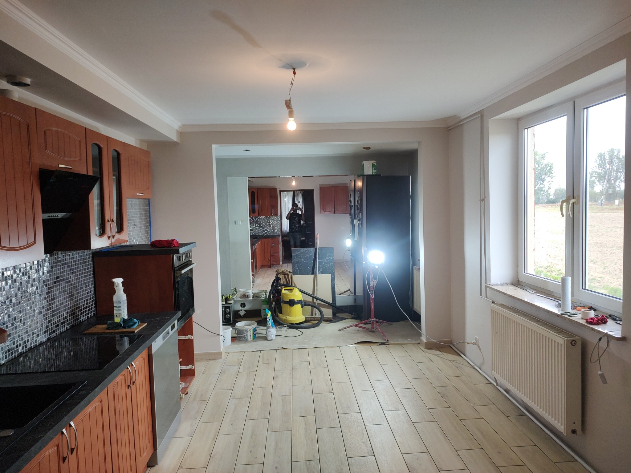 Remont kuchni z widocznymi narzędziami i sprzętem budowlanym. Ułożone płytki podłogowe, w tle widoczne szafki kuchenne. Całość oświetlona lampą budowlaną.