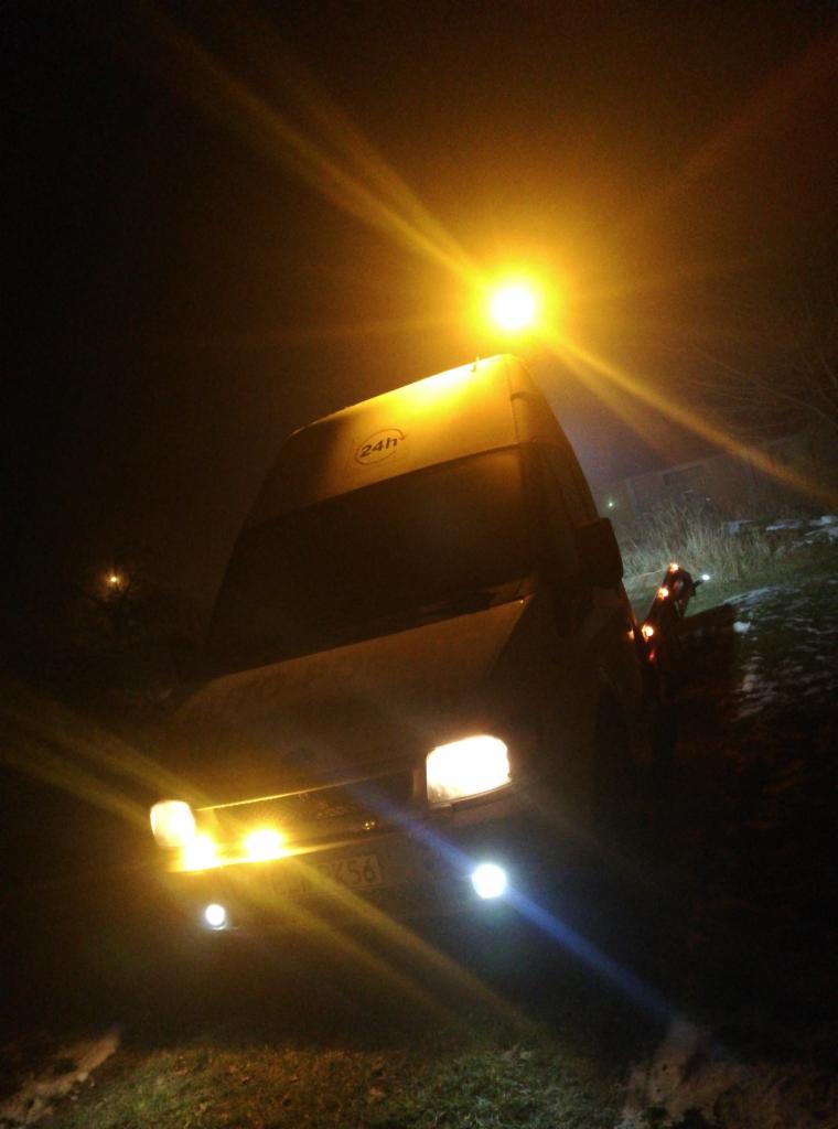 Nocne ujęcie lawety z włączonymi światłami awaryjnymi i oświetleniem roboczym, widoczne oznaczenie 24h na nadwoziu, teren trawiasty z resztkami śniegu.