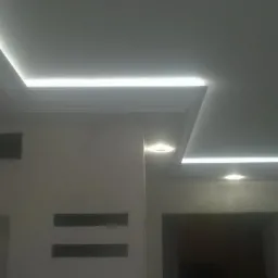 Nowoczesny sufit podwieszany z oświetleniem LED w kształcie litery L, z dekoracyjną listwą przysufitową i punktowymi lampami halogenowymi.