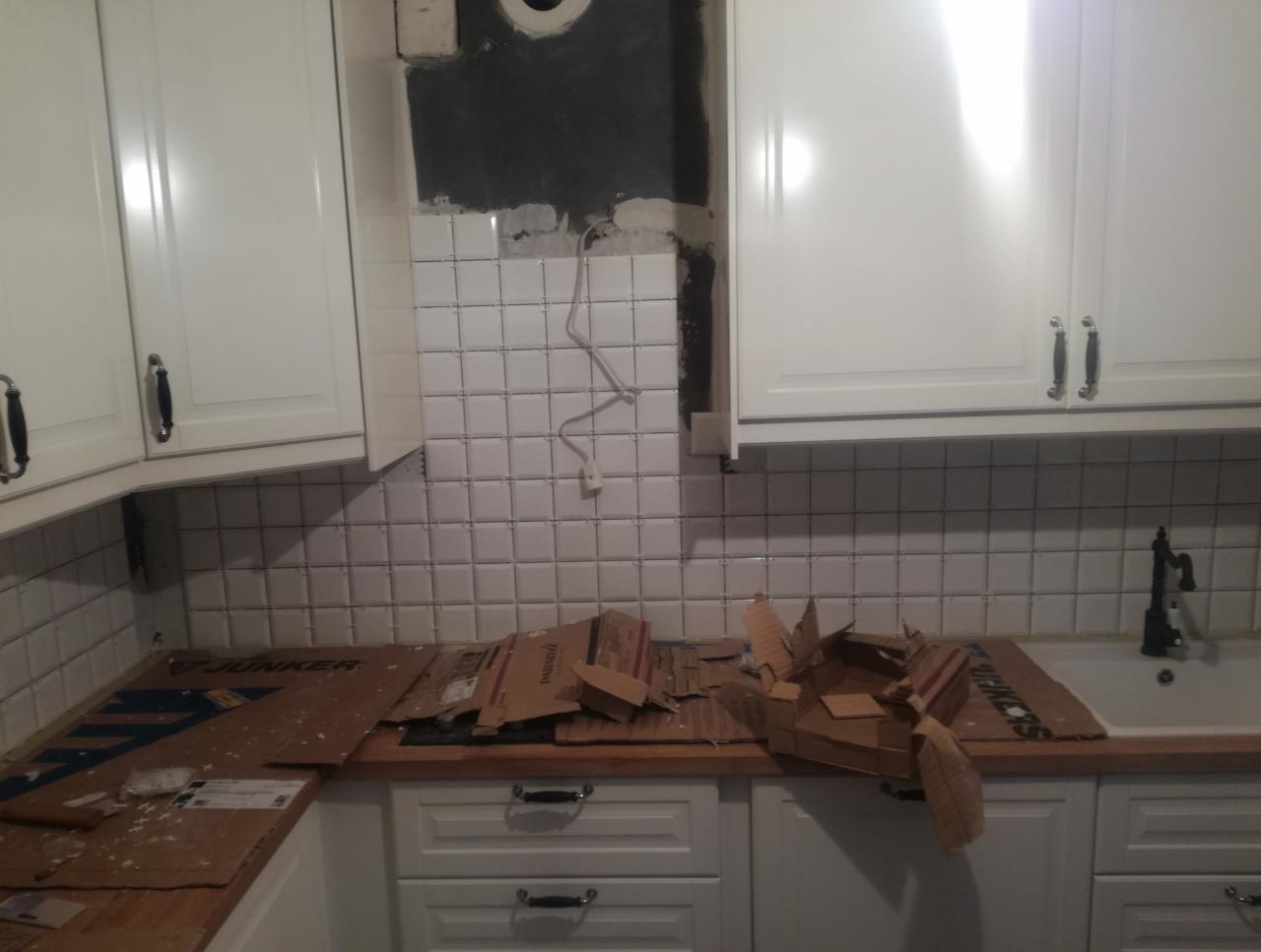 Wnętrze kuchni w trakcie remontu w Rzeszowie: częściowo położone białe płytki na ścianie nad blatem, białe szafki wiszące i stojące, zabezpieczony blat kartonem, widoczne niedokończone prace przy...