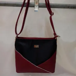 Dwukolorowa torebka damska, czarno-bordowa, z ukośnym zamkiem błyskawicznym, zawieszona na metalowym wieszaku.