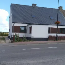 Wykończony dom jednorodzinny z szarą dachówką i białymi ścianami, z brązowymi akcentami wokół okien, widok z ulicy.