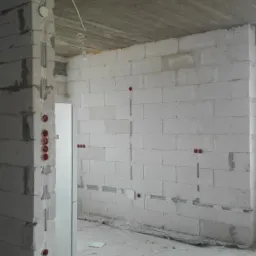 Wnętrze w stanie surowym z widocznymi instalacjami elektrycznymi w ścianach z betonu komórkowego, kable prowadzone po suficie.