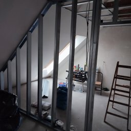 MIX MIR USŁUGI REMONTOWO WYKOŃCZENIOWE MIROSŁAW KALINKA - Metalowa konstrukcja szkieletowa pod zabudowę ścianki działowej na poddaszu, widoczne narzędzia i materiały budowlane, okno dachowe w tle.