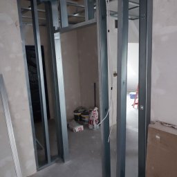 MIX MIR USŁUGI REMONTOWO WYKOŃCZENIOWE MIROSŁAW KALINKA - Metalowa konstrukcja ścian działowych z płyty karton-gips w trakcie montażu, widoczne profile pionowe i poziome, worki z zaprawą i wiaderka z farbą w tle, przewody elektryczne przymocowane do profili.